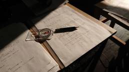 画像: 机の上に置かれたコンパスと鉛筆、手書きのメモが重なる静かな作業空間の写真です。光と影が強調され、集中の場面を表現