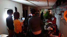 画像: 室内撮影現場で、数人のスタッフがカメラを調整しています。暗めのリビングルームで、窓の外が映り込んでいます。関連キーワード: 映画