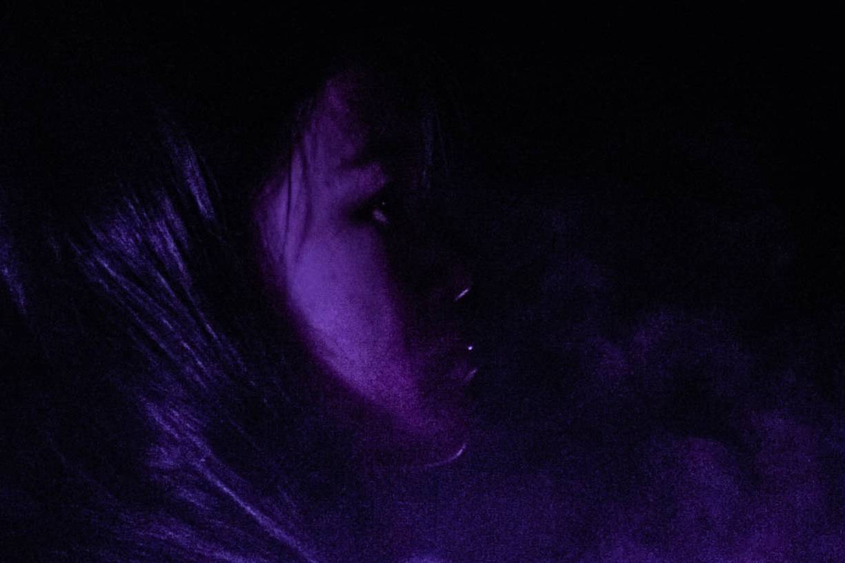 画像: この画像は、暗い背景に紫色のライトで照らされた女性の横顔を描写しています。神秘的で幻想的な雰囲気があります。「ポートレート」「暗闇」「紫色の