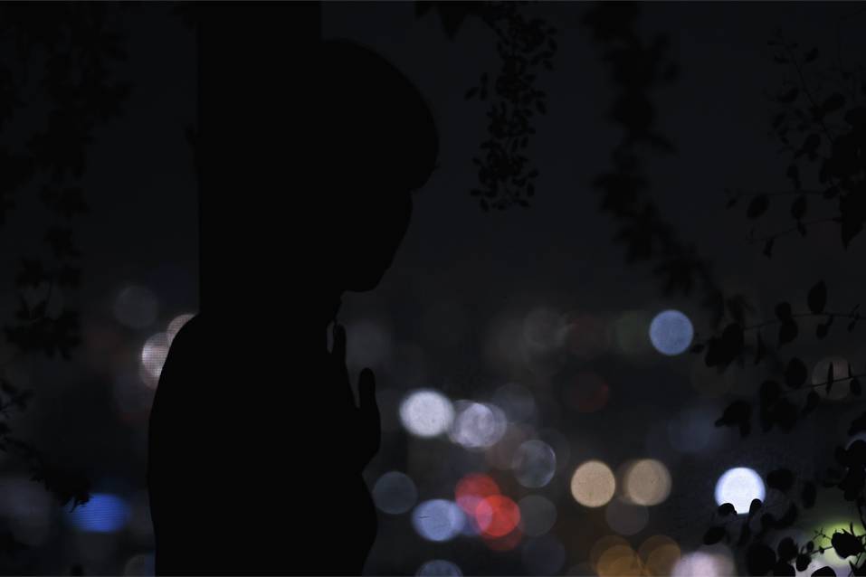 画像: この画像は、夜景を背景に、シルエットになった人物が佇むシーンを描写しています。背景のボケが美しい都会の夜景を演出しており、静寂と