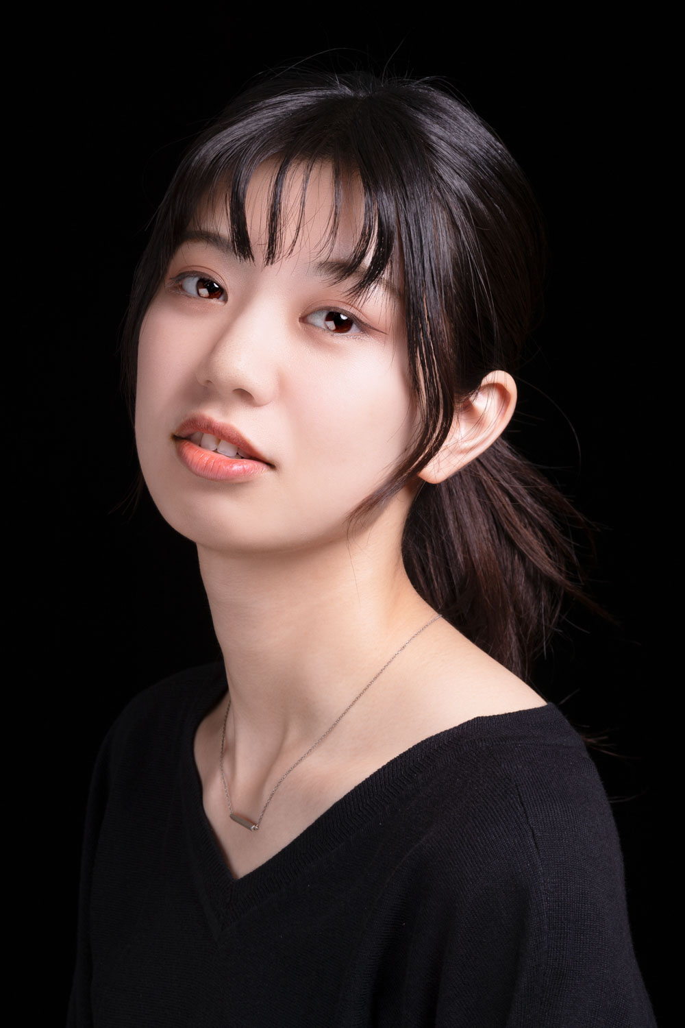 画像: この画像は、黒い背景に若い女性のポートレートです。彼女はシンプルな黒いトップスを着ており、落ち着いた表情をしています。主なキーワード: ポ
