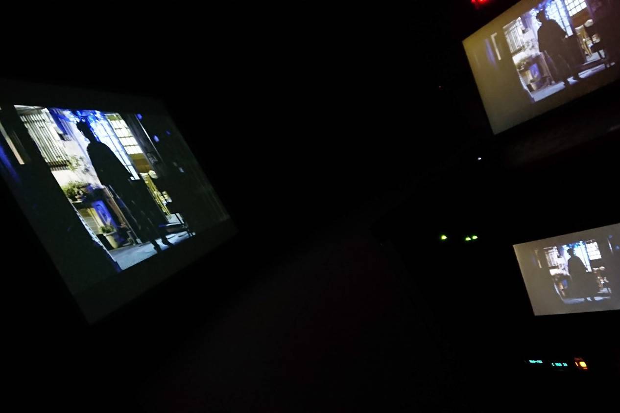 画像: 暗い室内で複数のスクリーンに映し出された映画のシーン。人影が窓の前に立つ場面が映し出されており、映画鑑賞の雰